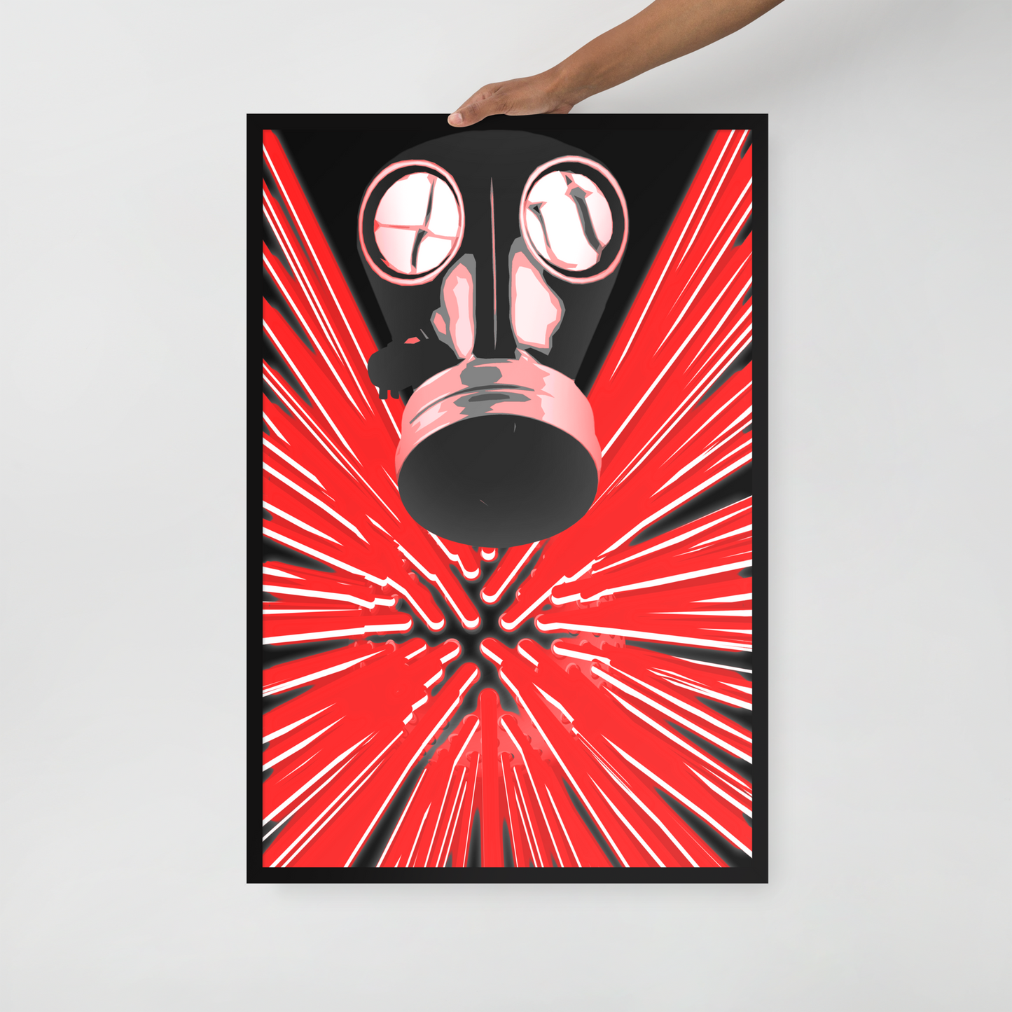 A framed art print featuring a stylized black gas mask over a bright red and black radial burst pattern, held against a light gray wall by a person's hand.