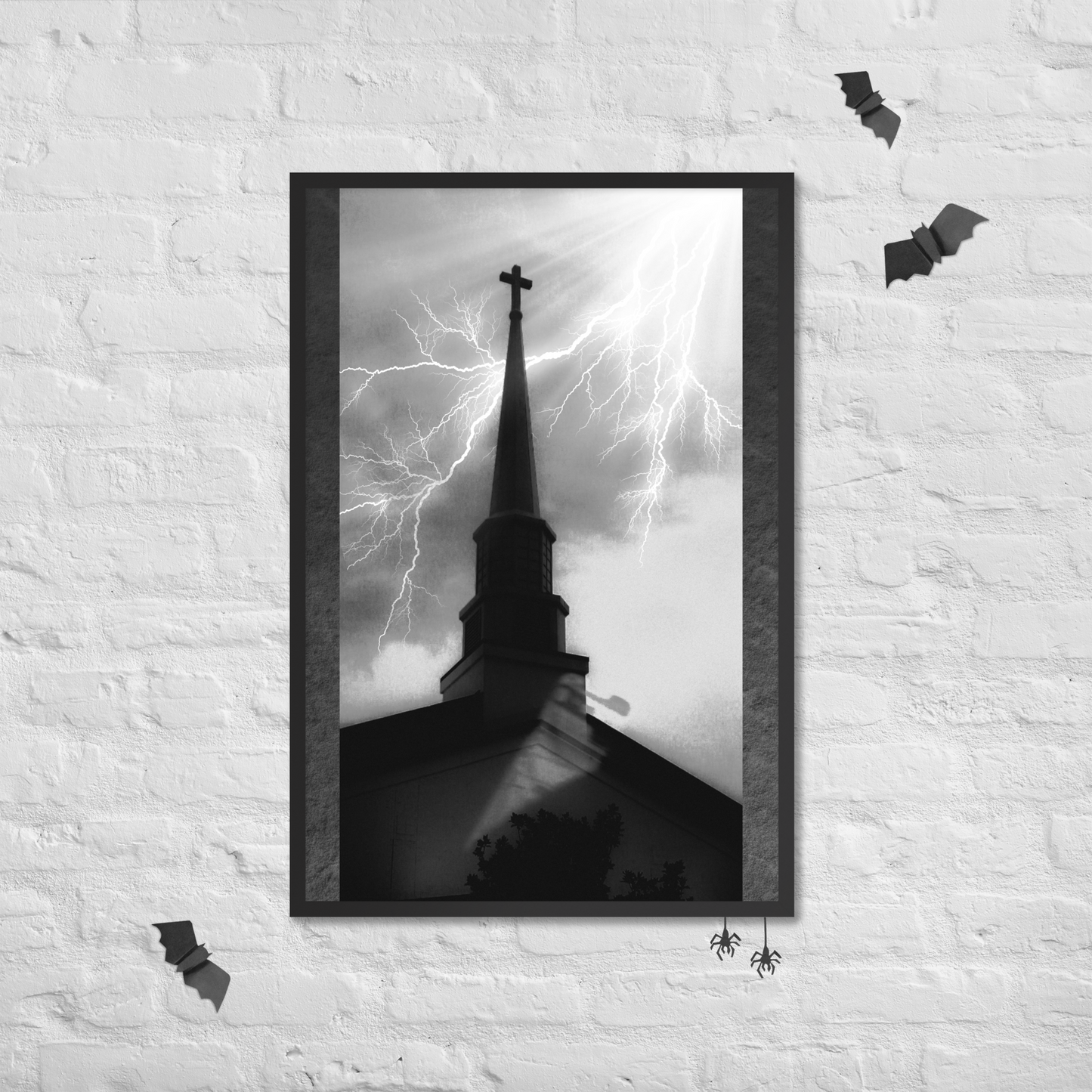 A framed black and white art print depicting a church steeple with lightning in the sky, displayed on a white brick wall with Halloween decorations.
